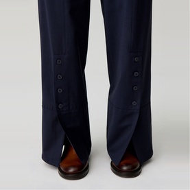 Model wearing Claude Pierlot Straight Leg Trousers in blue, showing front ankle slits with button placket detail and tonal lacquered buttons.