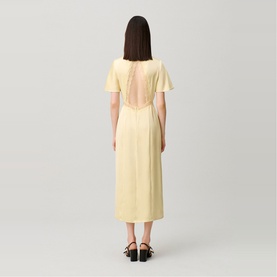 Model wearing Claude Pierlot Lace Slit Dress in baby yellow, showing open lace back detail, midi length, short sleeves, styled with black sandals