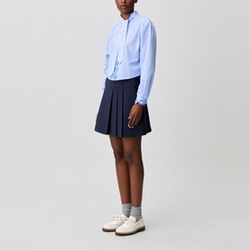 Model wearing Claude Pierlot Asymmetric Pleated Mini Skirt in blue, styled with a light blue shirt and white loafers.