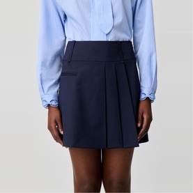 Model wearing Claude Pierlot Asymmetric Pleated Mini Skirt in blue with flat pleats, thick waistband, styled with a light blue shirt.