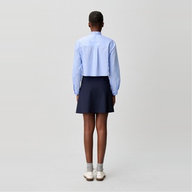 Model wearing Claude Pierlot Asymmetric Pleated Mini Skirt in blue, styled with a light blue cropped shirt and white trainers.