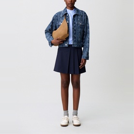 Model wearing Claude Pierlot Asymmetric Pleated Mini Skirt in blue, styled with a printed denim jacket and camel crossbody bag.