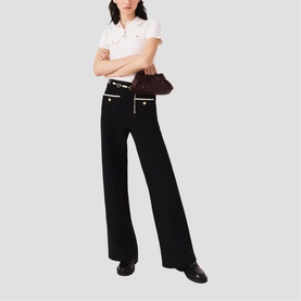Model wearing Maje red wide-leg trousers with gold-tone button details, styled with a white polo shirt and black loafers, carrying a brown bag.