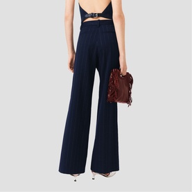 Model wearing Maje wide-leg navy pinstripe trousers with a backless top and belt, styled with strappy heels, carrying a brown fringed bag.