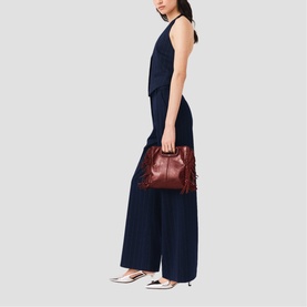 Model carrying a burgundy leather fringe shoulder bag, styled with a navy sleeveless wide-leg jumpsuit and white flat shoes.