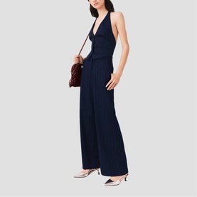 Model wearing Maje navy halterneck wide-leg jumpsuit with pleated trousers, styled with a burgundy crossbody bag and silver heels