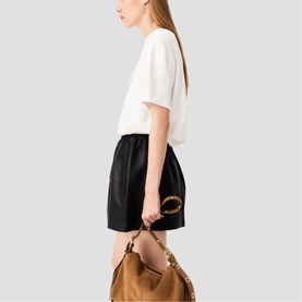 Model carrying Maje metallic hobo bag with bamboo-style ring handle and chain strap, styled with white tee and black mini skirt