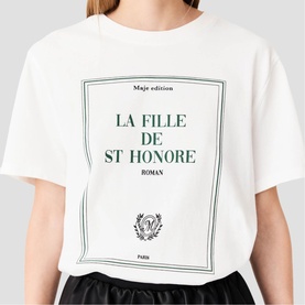 Model wearing Maje white graphic T-shirt with green "La Fille de St Honor&eacute;" book-cover print, styled with black skirt.