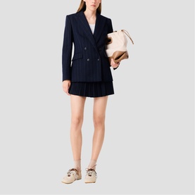 Model wearing Maje Womens French Dress in navy, double-breasted blazer style with pleated mini skirt, styled with cream bag and lace-up flatforms