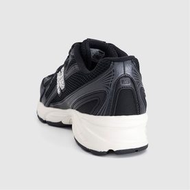 New Balance trainer in black, featuring mesh and overlay panelling, NB logo detail, and off-white chunky sole. Rear view.