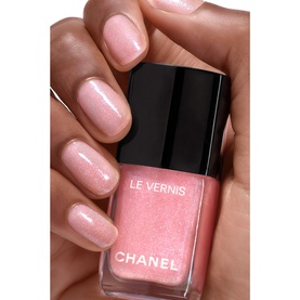 Chanel Le Vernis nail varnish in 421 Cristalline, a shimmering pink pearl shade, held and worn on manicured nails