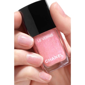 Chanel Le Vernis nail varnish in 421 Cristalline, sheer pink shimmer formula shown held between fingers with matching manicure