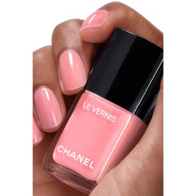 Chanel Le Vernis nail varnish in 421 Cristalline, a soft coral pink, shown applied to nails alongside the bottle