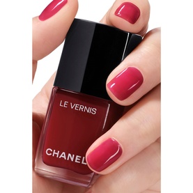Chanel Le Vernis nail varnish in 421 Cristalline, deep berry-red shade, shown applied on model's hand beside the bottle