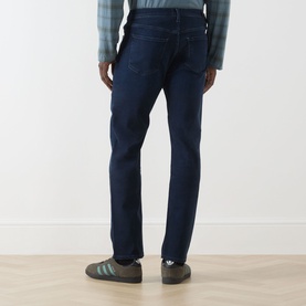 Model wearing Citizens of Humanity blue straight jeans, rear view, styled with a plaid shirt and green trainers.