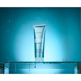 Color Wow Money Laundering Conditioner tube displayed upright on glass surface with water droplets against teal background