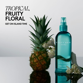 Fenty Skin Body Mist in teal spray bottle, styled with a pineapple and tropical flowers on a reflective surface