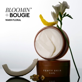 Fenty Skin Amber Bouquet Butta Drop Whipped Oil Body Cream open jar showing cream texture, styled with white florals and lemon