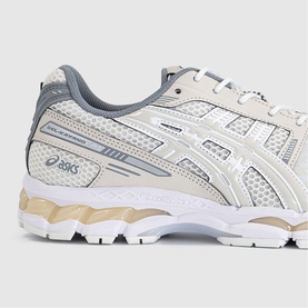 Asics Gel-Kayano trainer in cream and smoke grey with gold midsole detailing and white outsole, angled side view
