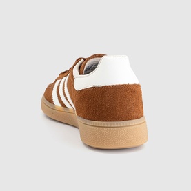 Adidas trainer in dusky bronze suede with white three-stripe detail, gum rubber sole, rear three-quarter view.