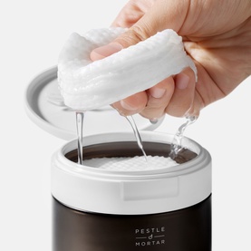 Pestle & Mortar Pore Reset Pads exfoliator pad being squeezed, releasing liquid into the refillable dark jar container