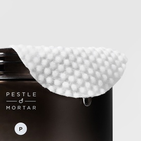 Pestle & Mortar Pore Reset Pads exfoliating treatment pad resting on dark brown bottle, showing textured white cotton surface.
