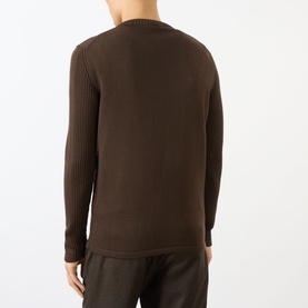 Model wearing Prada brown virgin wool crew neck jumper, back view showing ribbed sleeve and hem detailing, styled with dark trousers.