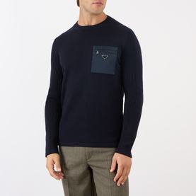 Model wearing Prada Triangle Logo Patch Pocket Sweater in blue wool, ribbed crew neck, nylon chest pocket with zip and triangle logo. Styled with