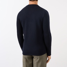 Model wearing Prada Triangle Logo Patch Pocket Sweater in blue, rear view showing ribbed sleeve detail and crew neckline, styled with khaki trousers.