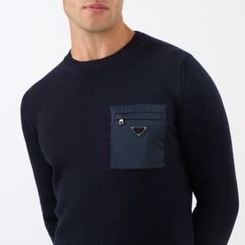 Model wearing Prada Triangle Logo Patch Pocket Sweater in blue wool knit with nylon chest zip pocket and silver triangle logo plaque