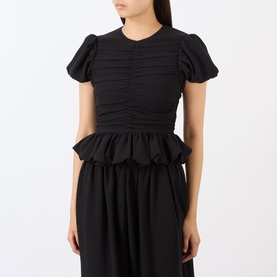 Model wearing Rotate black ruched short puff sleeve top with scalloped peplum hem, paired with a black midi skirt.