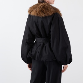 Model wearing Rotate black jacket, rear view, balloon sleeves, belted waist, brown faux fur collar trim, with black wide-leg trousers