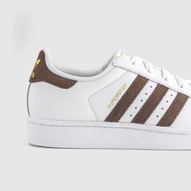 Adidas Superstar trainer in white with earth brown suede three stripes, shell toe, and white sole with gold branding detail.