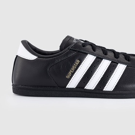 Adidas Superstar trainer in black leather with white three stripes, gold foil branding, and black sole