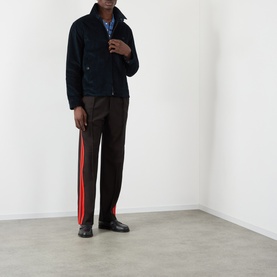 Model wearing Wales Bonner Drew Logo Corduroy Jacket in navy, styled with brown stripe trousers and black shoes.