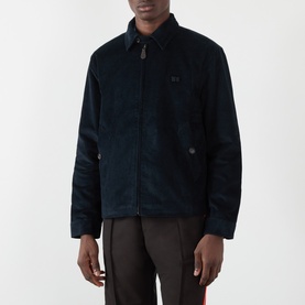 Model wearing Wales Bonner Drew Logo Corduroy Jacket in navy, with point collar, front zip fastening and welt pockets, styled with dark trousers.