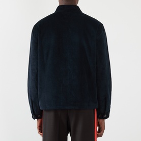 Model wearing Wales Bonner Drew Logo Corduroy Jacket in navy, rear view, styled with dark trousers featuring red side stripe detail.