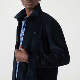 Model wearing Wales Bonner Drew Logo Corduroy Jacket in navy, styled open to reveal blue check print lining, with tonal logo embroidery visible on