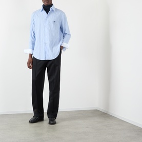 Model wearing Wales Bonner Atlantic Logo Striped Shirt in cornflower blue, styled with black straight-leg trousers and black loafers.