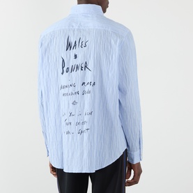Model wearing Wales Bonner Atlantic Logo Striped Shirt in cornflower blue, rear view showing handwritten logo script embroidery on striped fabric.