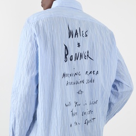 Model wearing Wales Bonner Atlantic Logo Striped Shirt in Cornflower Blue, rear view showing navy logo script embroidery on striped fabric.