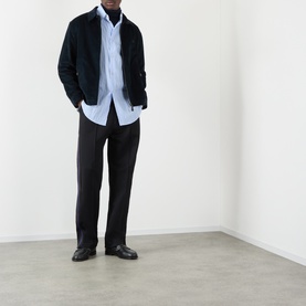 Model wearing Wales Bonner Atlantic Logo Striped Shirt in cornflower blue, styled with a dark jacket and black trousers.