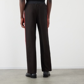 Model wearing Wales Bonner Energy Logo Track Pants in Brown/Black, straight-leg with contrast side stripe, paired with black loafers.