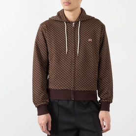 Model wearing Wales Bonner Brown/Caramel zip-up hoodie with allover jacquard pattern, white drawstrings, styled with black trousers.