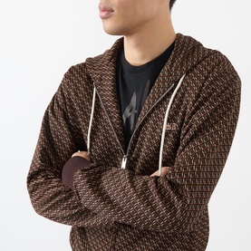 Model wearing Wales Bonner brown and caramel monogram zip-up hoodie with drawstring hood, styled with a black graphic T-shirt underneath.