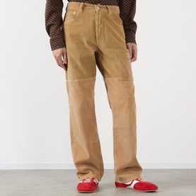 Model wearing Wales Bonner camel cotton chinos with panelled detailing, styled with red loafers and a patterned brown top.
