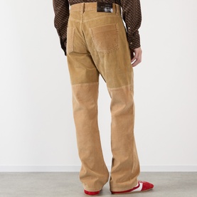 Model wearing Wales Bonner camel corduroy chinos, rear view, styled with brown patterned top and red trainers.