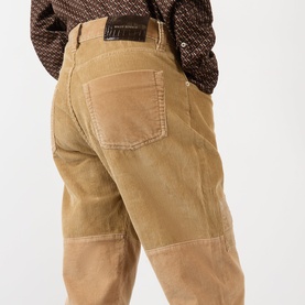 Model wearing Wales Bonner camel corduroy chinos, rear view, styled with a brown patterned shirt. Patch detailing on knees.