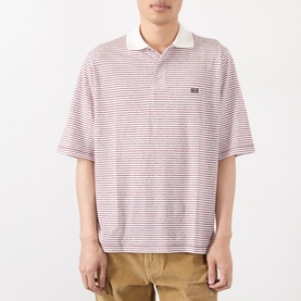 Model wearing Wales Bonner polo in ivory and wine horizontal stripes, white collar, small logo patch, styled with tan trousers.