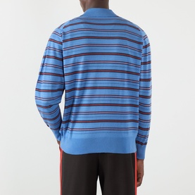 Model wearing Wales Bonner Beam Logo Striped Polo Sweater in chambray blue with multicolour stripes, long sleeves and ribbed trims, back view.